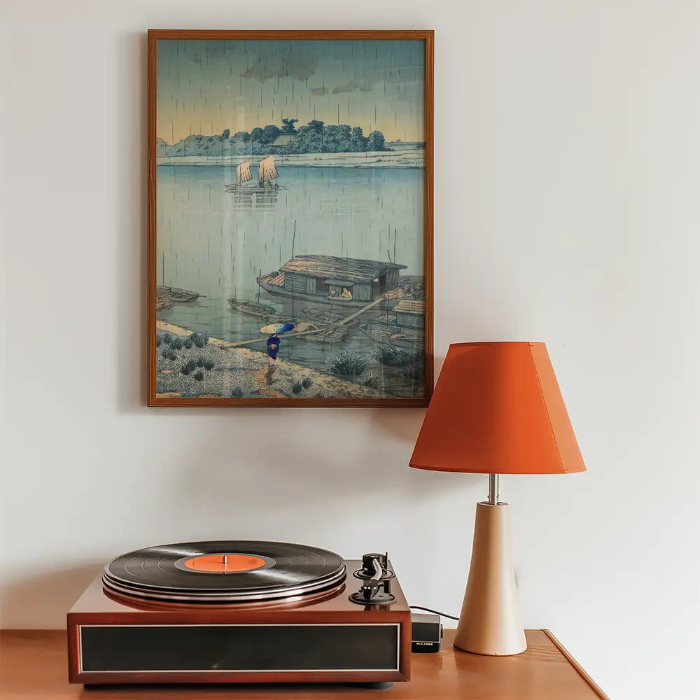 Framed painting of a serene landscape featuring boats on water, accompanied by a retro record player and orange lamp.
