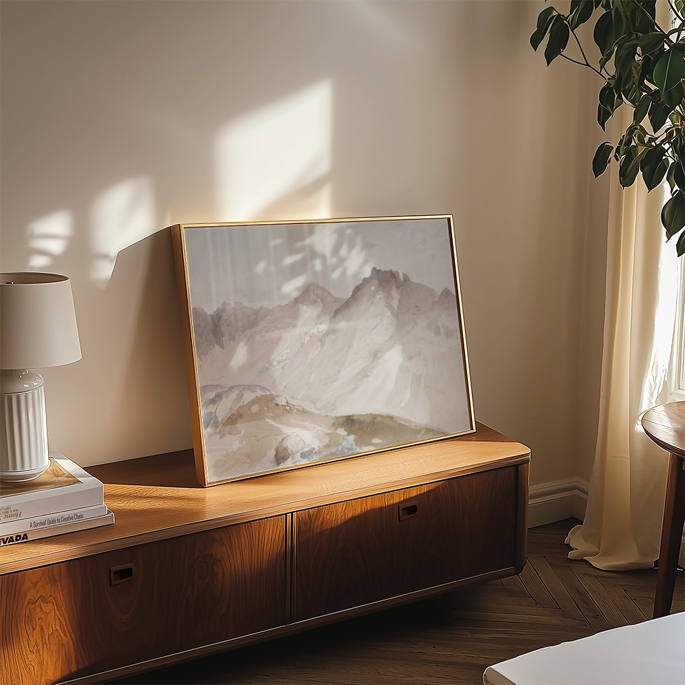 Framed abstract mountain landscape painting displayed on a wooden table near a lamp and plant in a sunlit room.