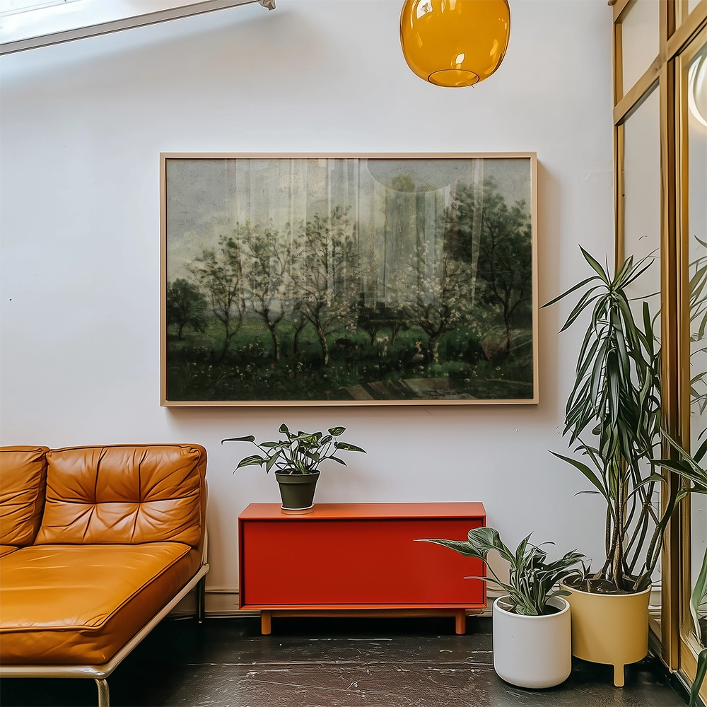 A framed landscape painting featuring trees and a green field, displayed in a modern living space with an orange couch and potted plants.