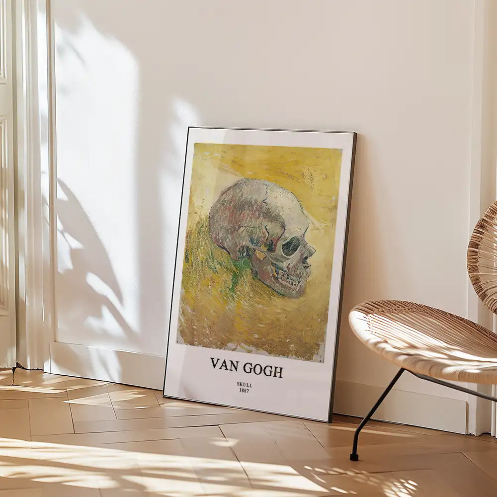 Framed painting of a skull by Van Gogh, titled "Skull," 1887, displayed on a wall next to a woven chair.