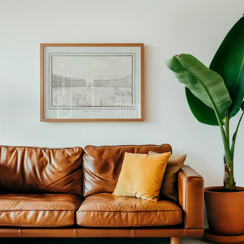 Framed artwork displayed above a brown leather couch with a yellow pillow and a large green plant in a pot.