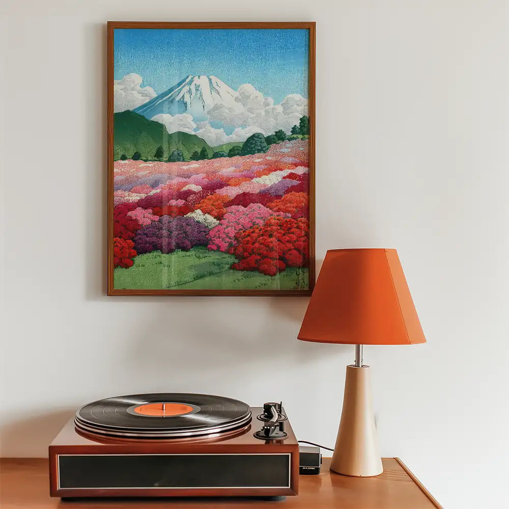 Framed painting of Mount Fuji surrounded by colorful flower fields, displayed above a vintage record player and an orange table lamp.
