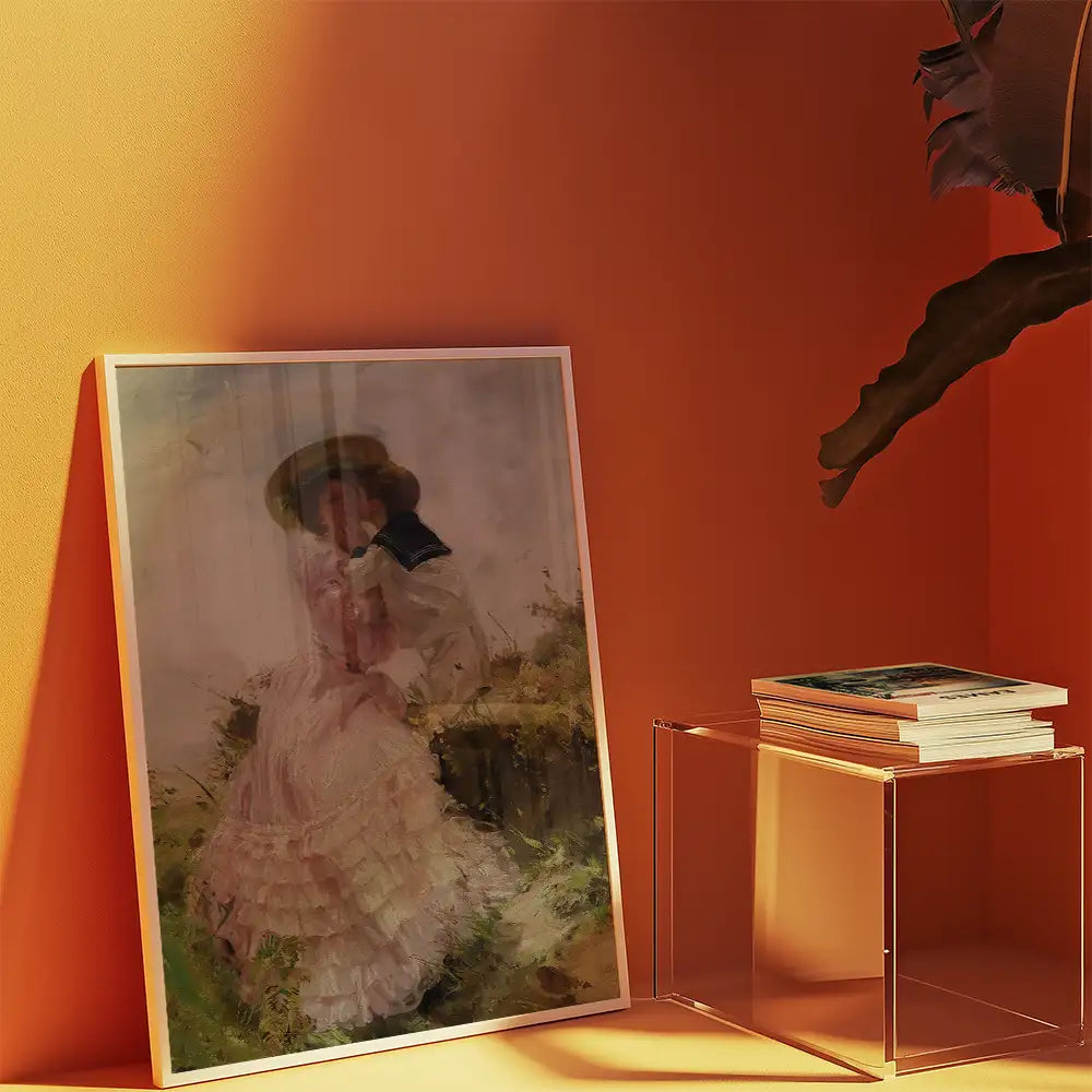 Framed painting of a woman in a white dress sitting in a garden, propped against a warm orange wall, with a clear display table holding stacked books.