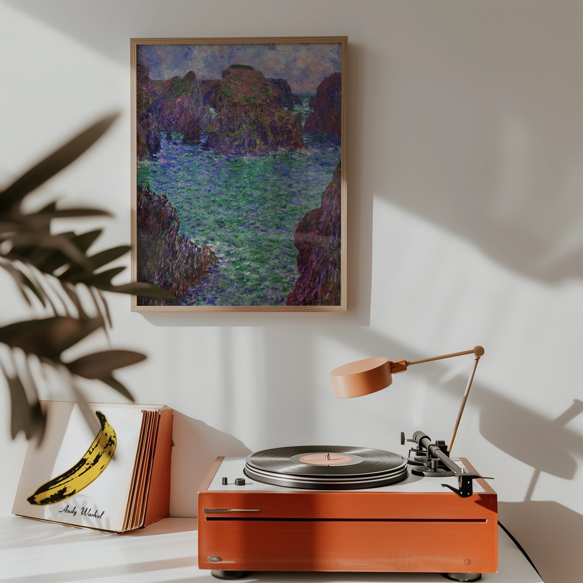 Framed painting of a serene coastal landscape featuring rocky outcrops and vibrant green water, displayed above a vintage record player in a stylish interior setting.
