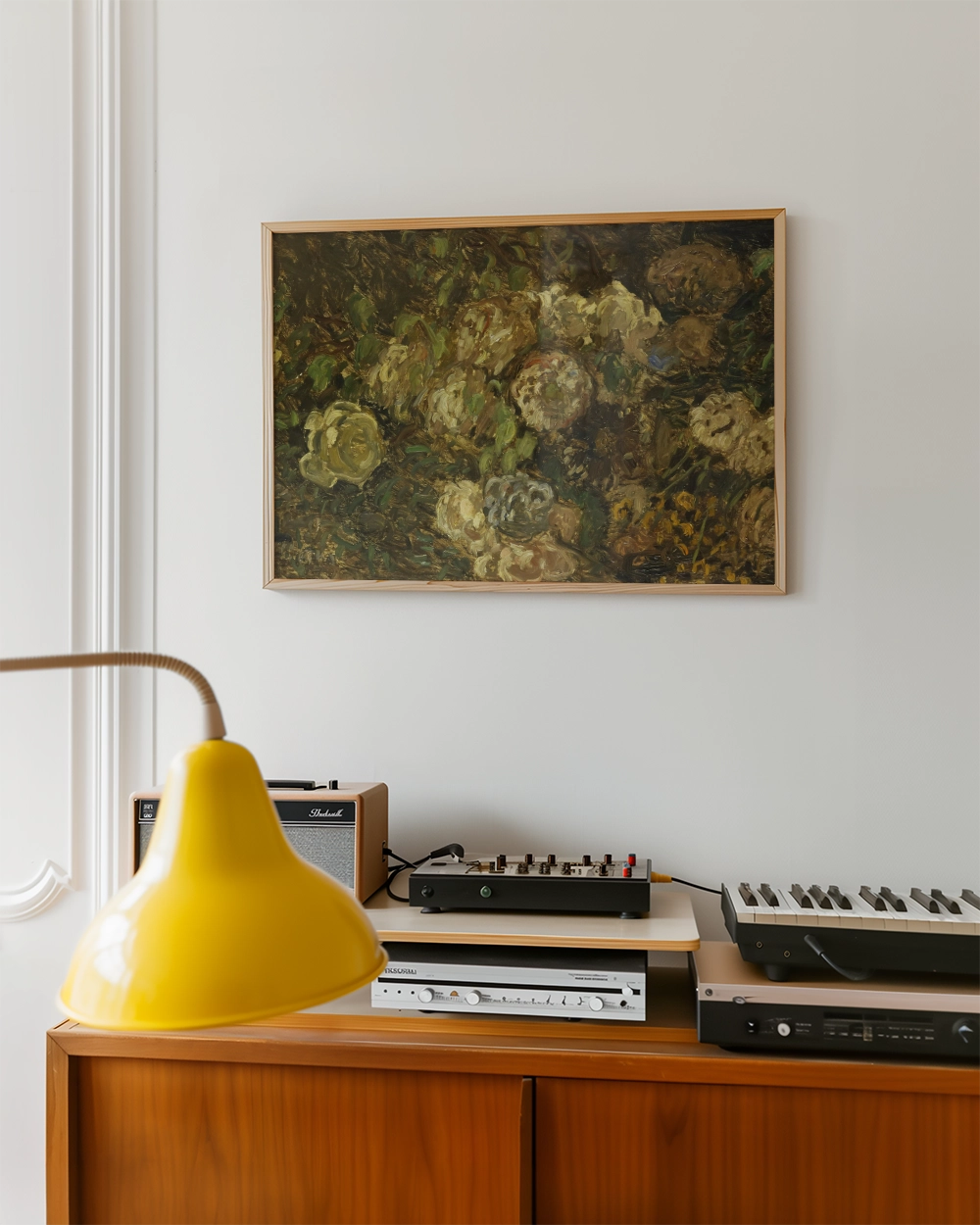 A framed painting of abstract flowers hanging on a white wall above a wooden cabinet with a yellow lamp and vintage audio equipment.