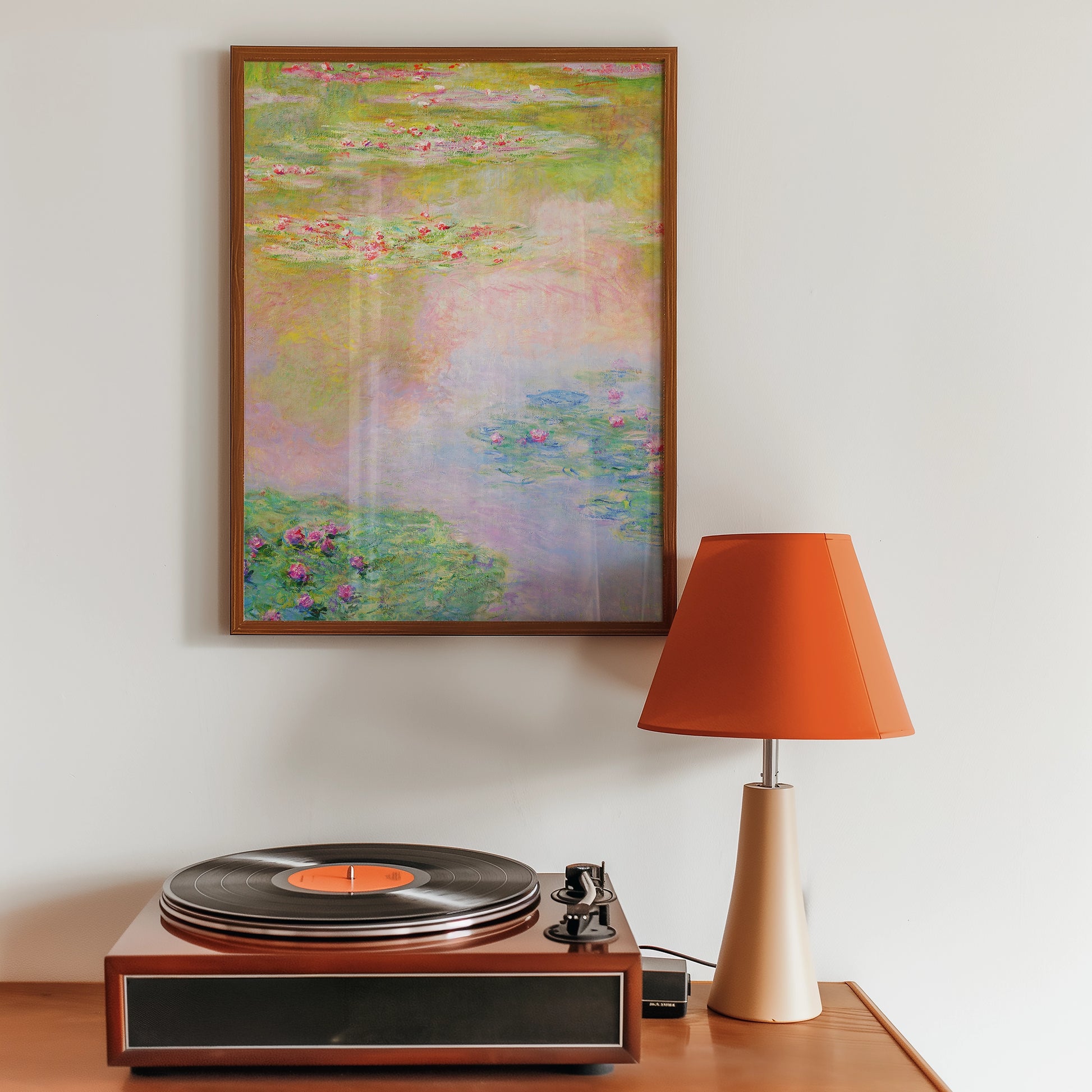 A framed painting of water lilies hanging on a wall beside a vintage record player and an orange lamp.