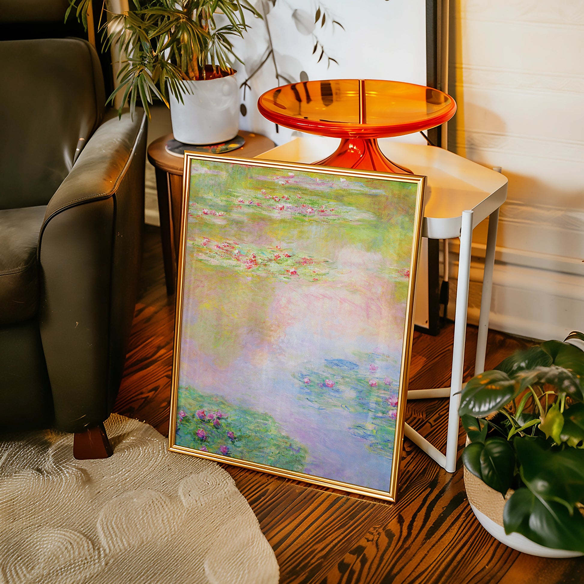 Framed painting of water lilies in soft pastel colors leaning against a chair in a cozy living space.