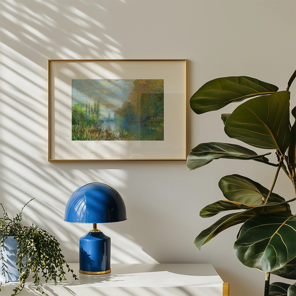 Framed landscape painting displayed on a wall with a blue lamp and plant in a modern interior setting.