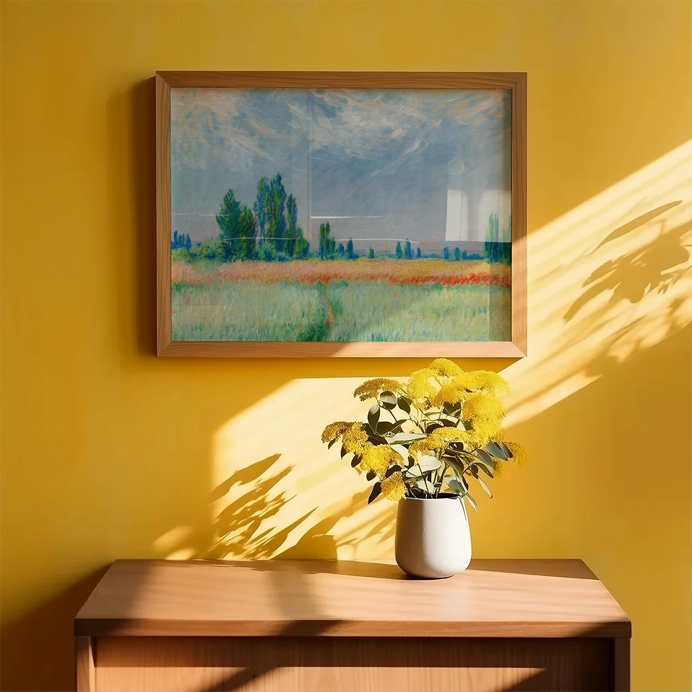 Framed painting of a serene landscape with green fields and trees, displayed on a yellow wall above a wooden table with a vase of yellow flowers.
