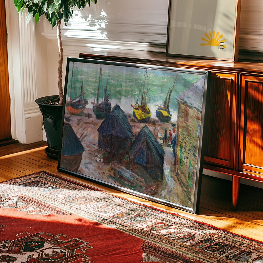 Framed painting of a coastal scene with fishing boats and huts, placed on a wooden floor beside a potted plant and decorative rug.