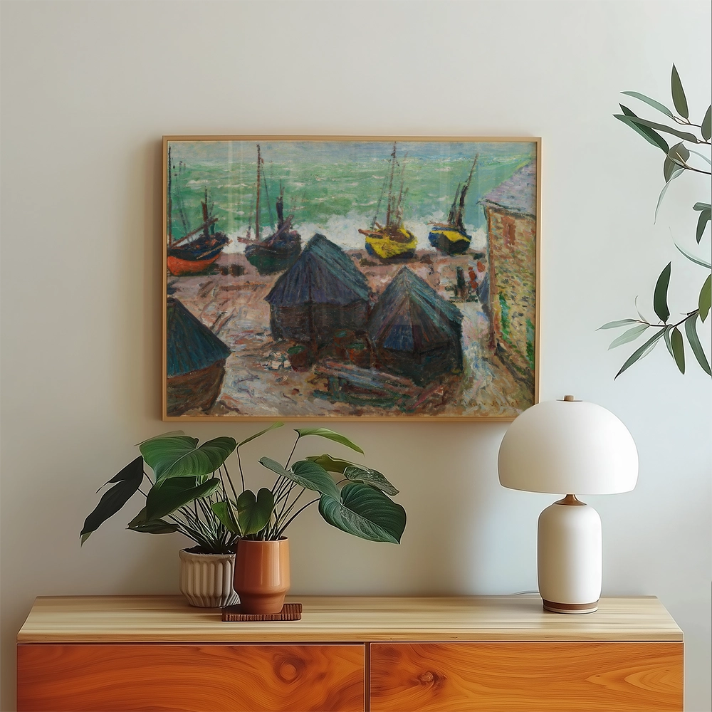 Painting of fishing boats and huts by the sea, displayed in a modern interior with a plant and lamp.
