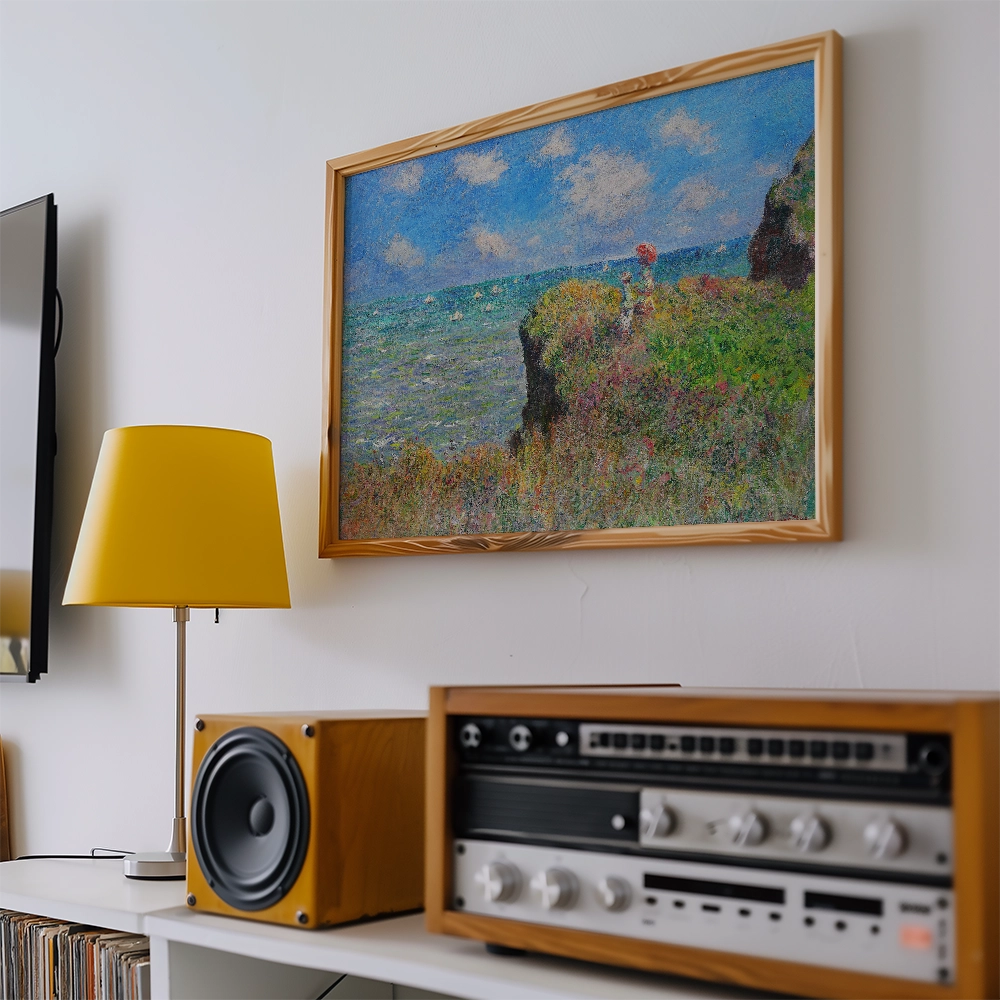 A colorful painting of a coastal landscape with blue skies and green hills, framed and hung on a white wall, accompanied by a yellow lamp and wooden audio equipment.
