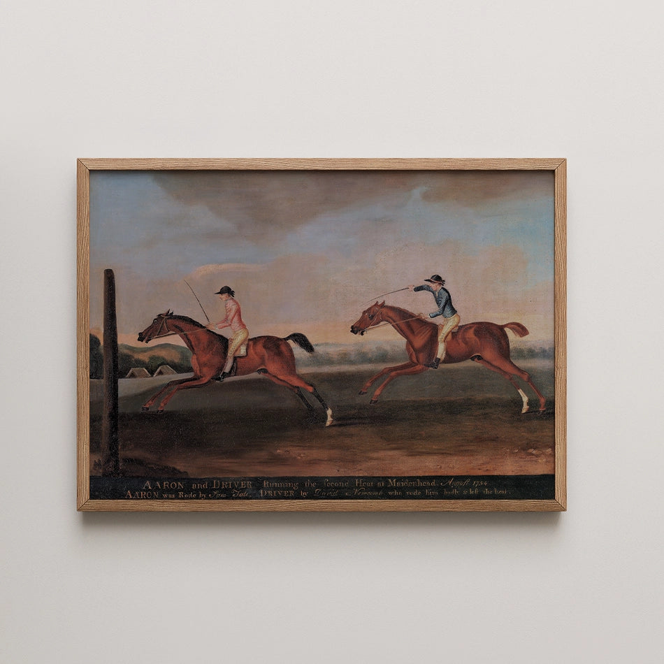 Painting of two horse racers competing, titled "Aaron and Driver," framed in light wood.