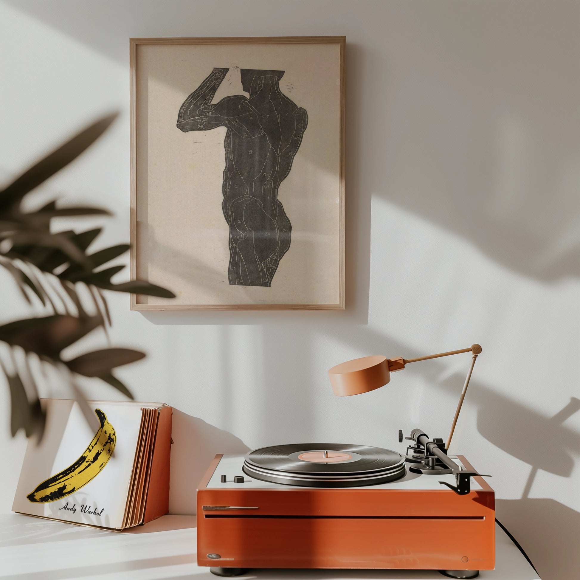 Framed art print of a stylized black figure on a light background, displayed above a vintage record player and an album cover featuring a banana design.