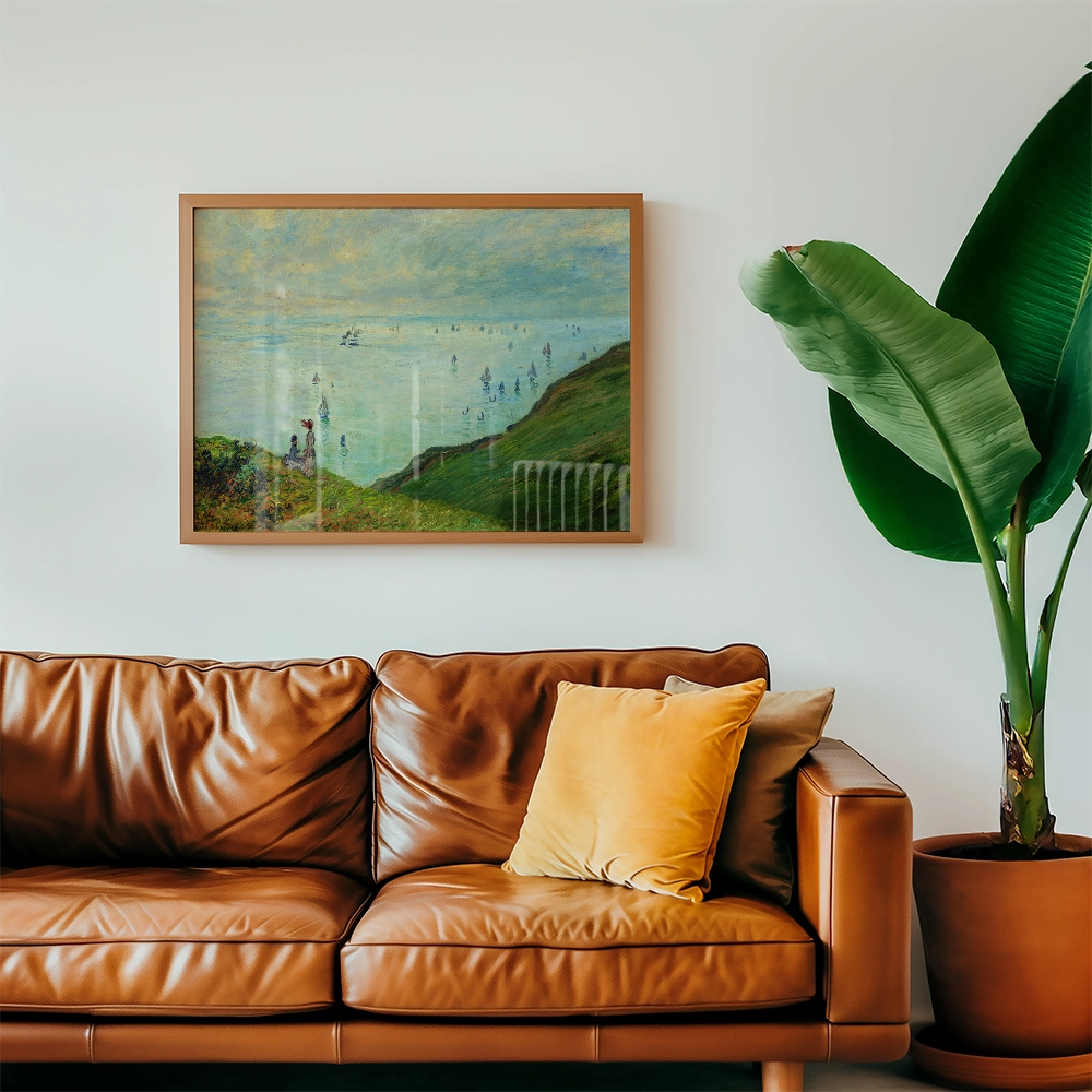 Framed painting of a coastal scene hanging above a brown leather sofa with cushions and a potted plant.