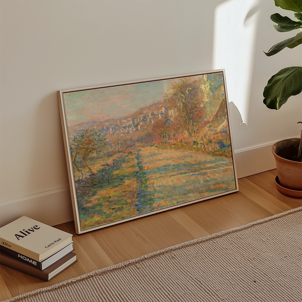 Painting of a serene landscape with hills and trees, framed and leaning against a wall alongside stacked books and a potted plant.