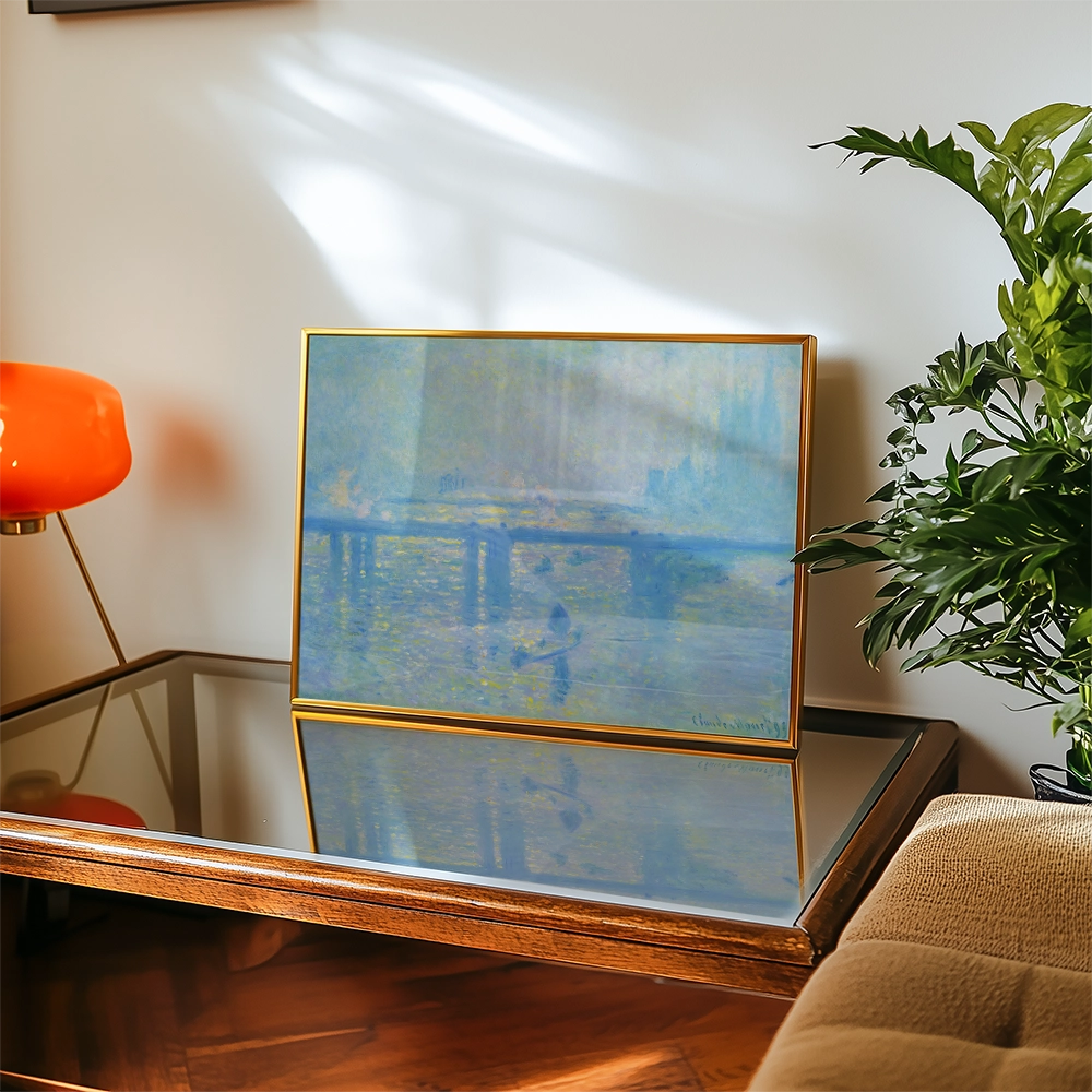 A decorative painting in a gold frame on a wooden table, with a soft blue and yellow color palette, accompanied by a vibrant orange lamp and green plant in a cozy living space.