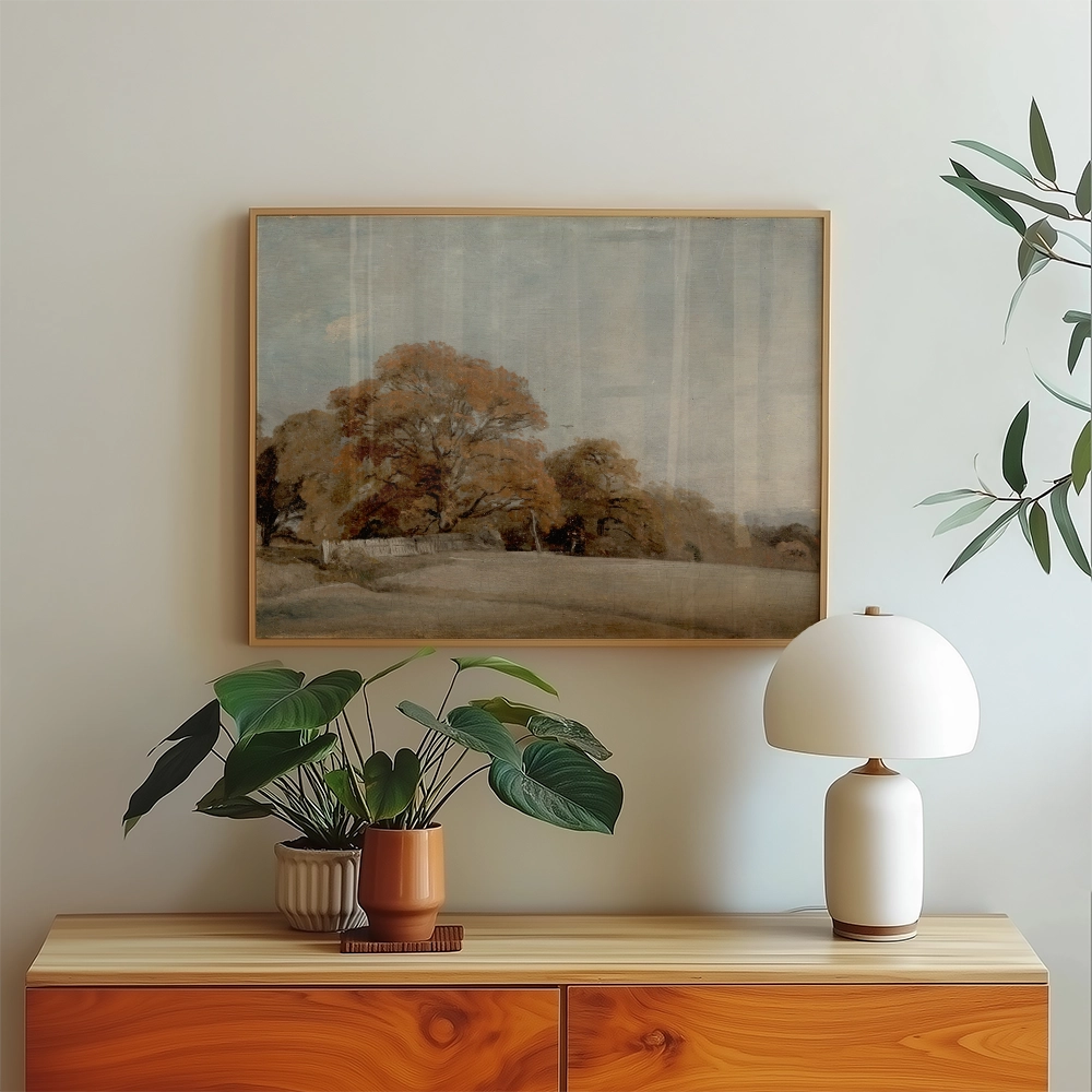 Framed landscape painting featuring autumn trees, displayed above a wooden sideboard with decorative plants and a lamp.