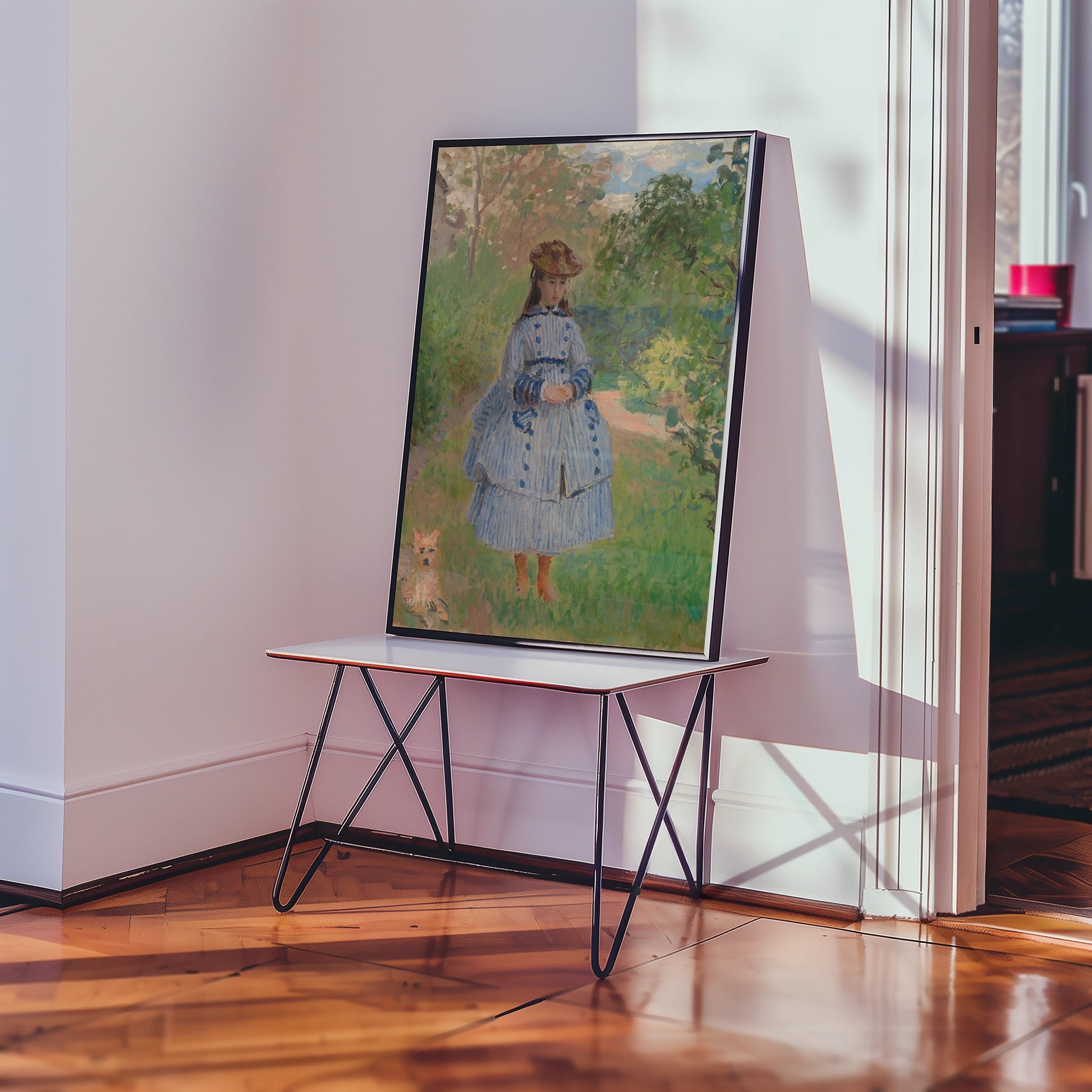 A framed painting of a girl in a blue dress standing in a garden, accompanied by a small dog, displayed on a minimalist table in a bright interior setting.