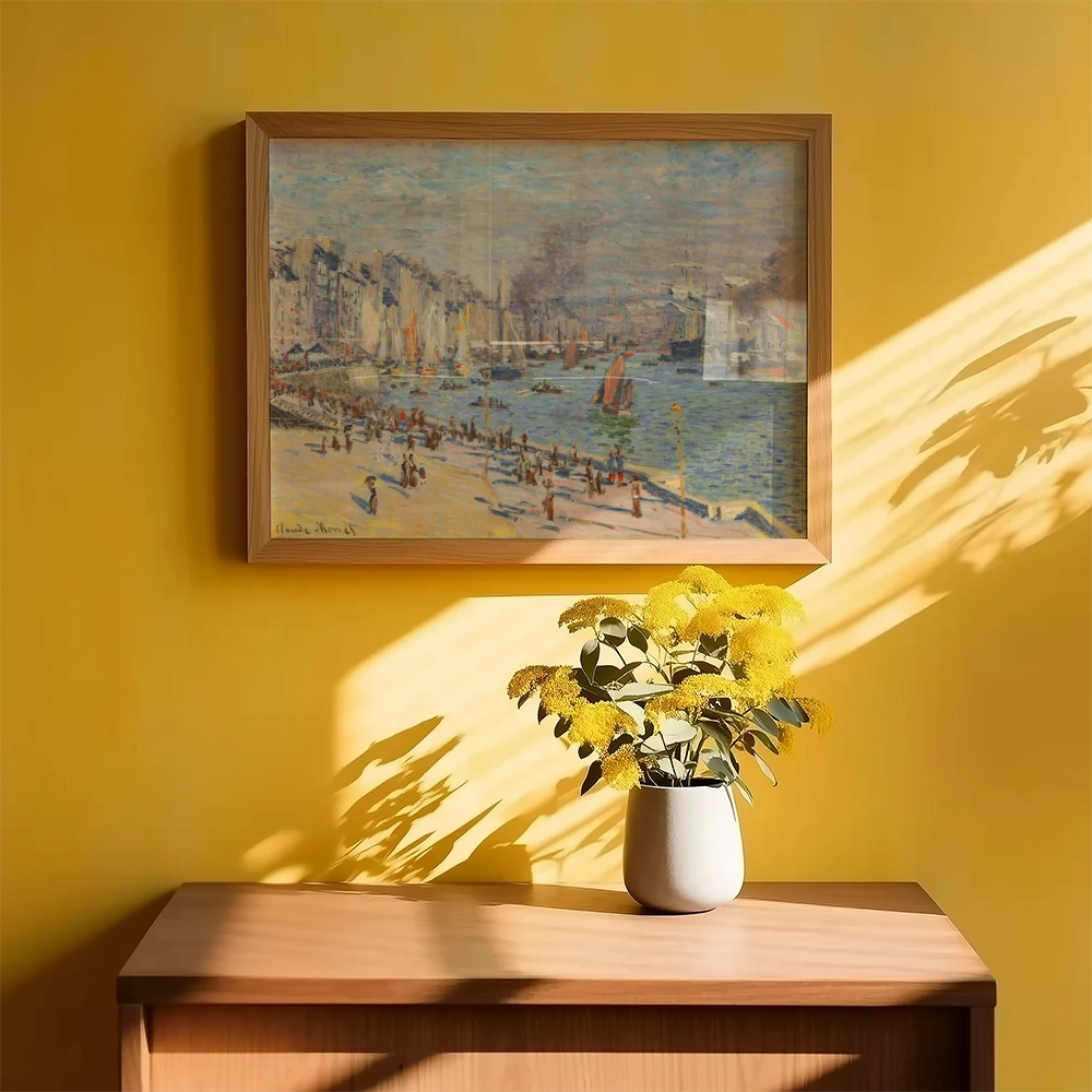 Framed painting of a coastal scene with boats and people on the beach, displayed on a yellow wall with a vase of yellow flowers on a wooden surface.