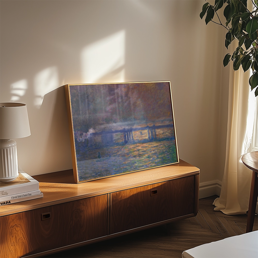 A tranquil painting featuring soft colors depicting a waterfront scene, elegantly framed and displayed on a modern wooden side table with a lamp and plant in a sunlit room.
