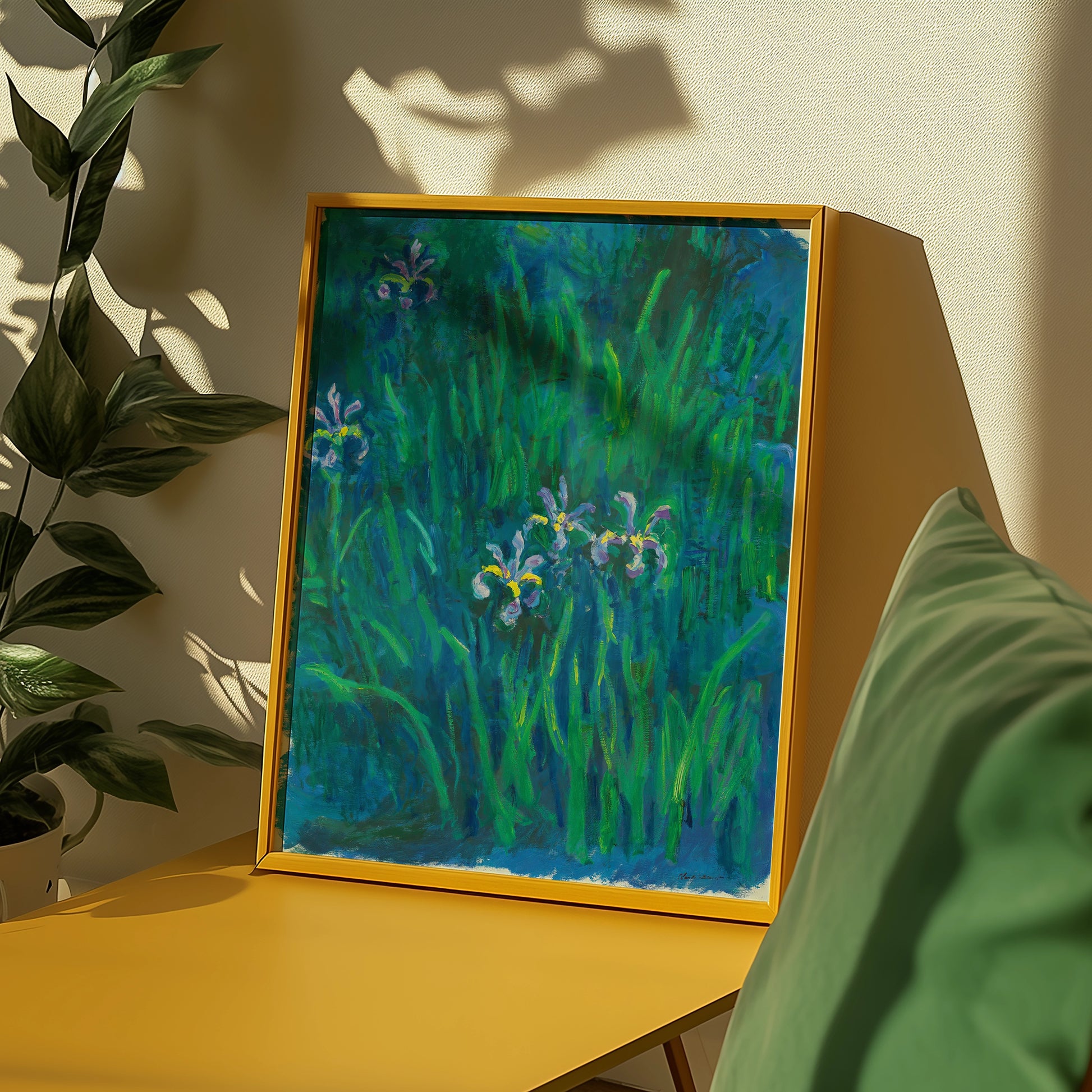 Framed painting of irises in green grass, displayed on a yellow table with a plant in the background.
