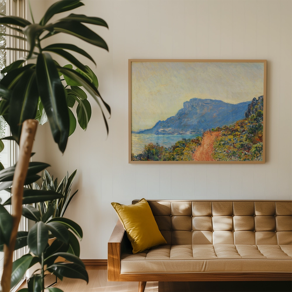 Painting of a coastal landscape with hills and a sea view, framed and displayed above a styled sofa with a yellow cushion, surrounded by indoor plants.
