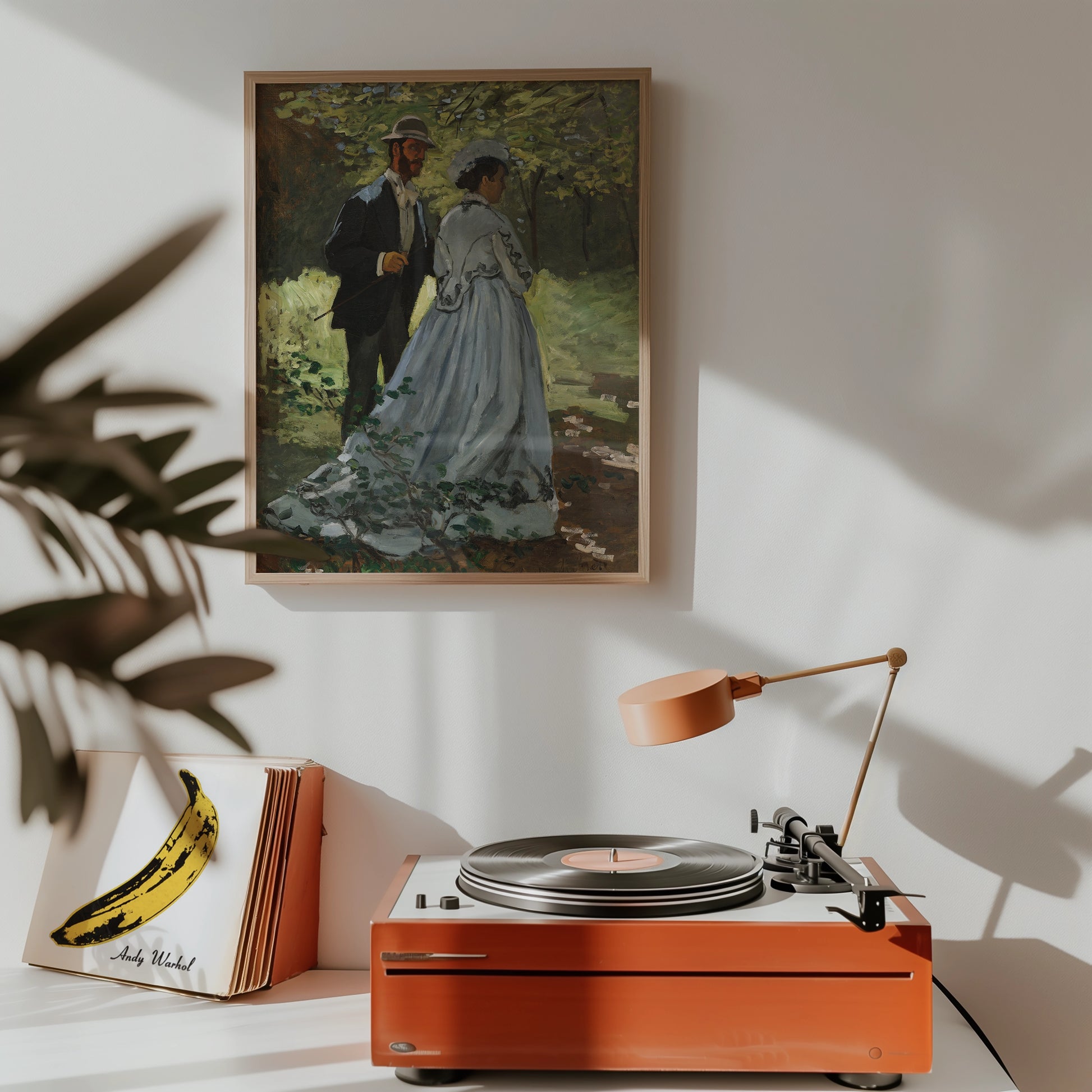 Painting of a couple in a park, framed and displayed on a wall above a record player and a stylish lamp.