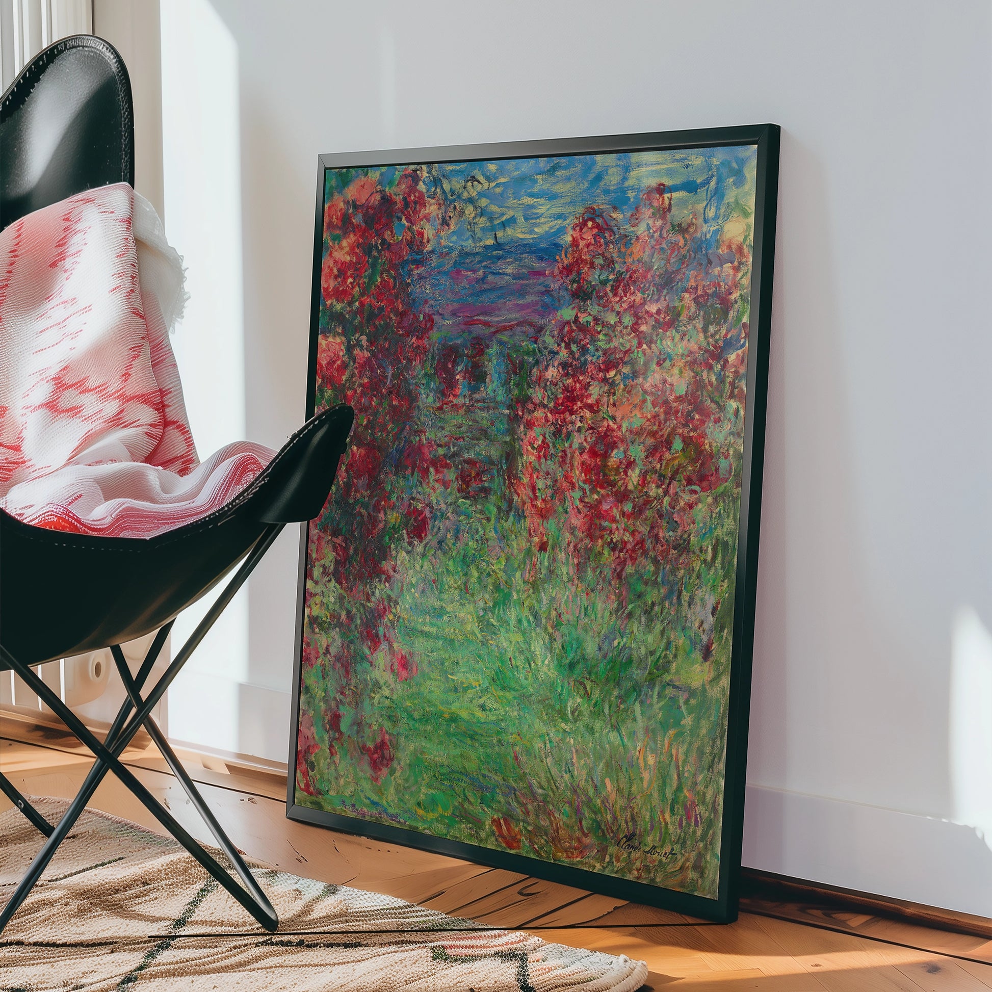 Colorful painting featuring vibrant red flowers and lush green foliage, displayed near a black chair in a well-lit interior setting.