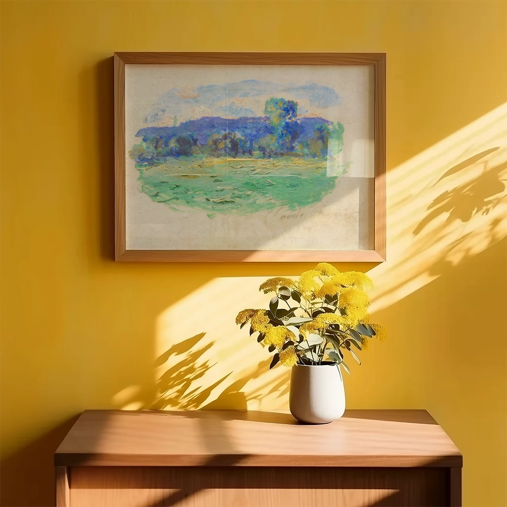 Framed painting of a serene landscape with shades of blue and green, hung on a yellow wall above a wooden table featuring a small vase of yellow flowers.