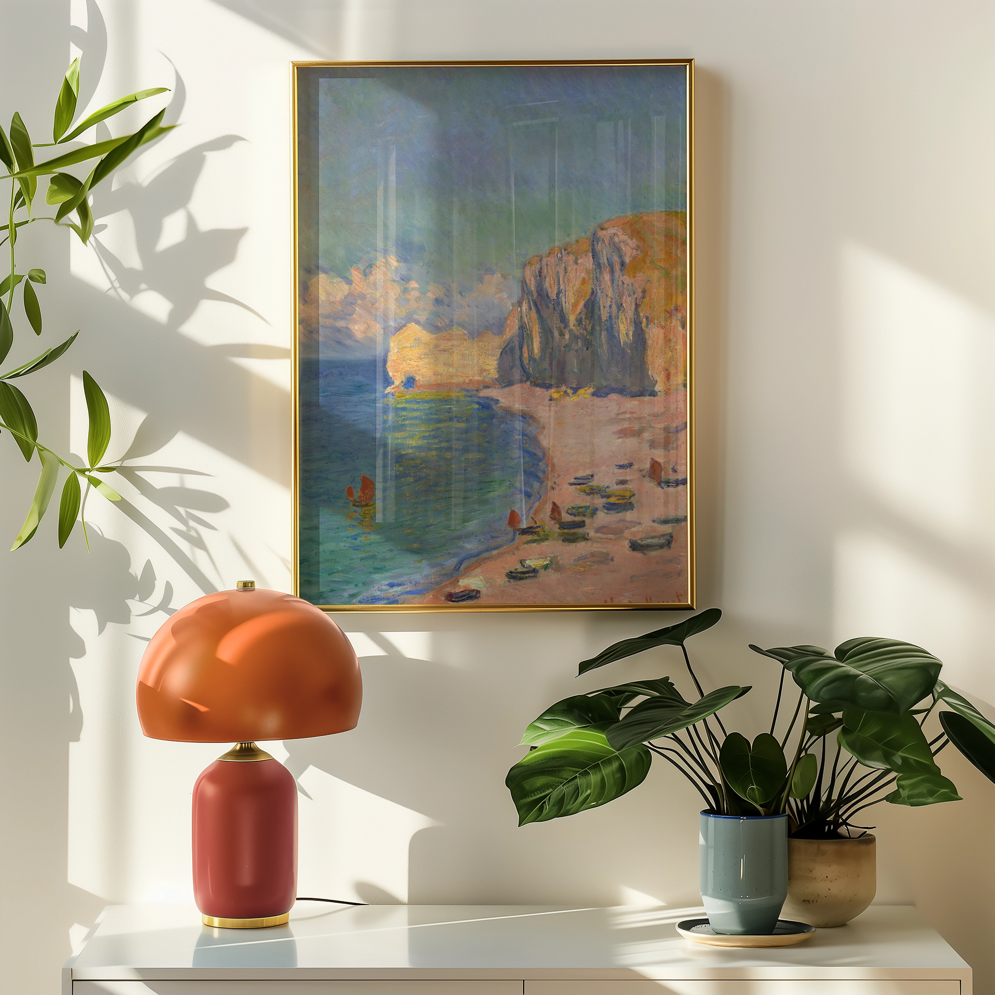 A vibrant painting of a beach scene with boats resting on the shore, framed in gold, displayed above a stylish red lamp and green plants in a sunlit room.