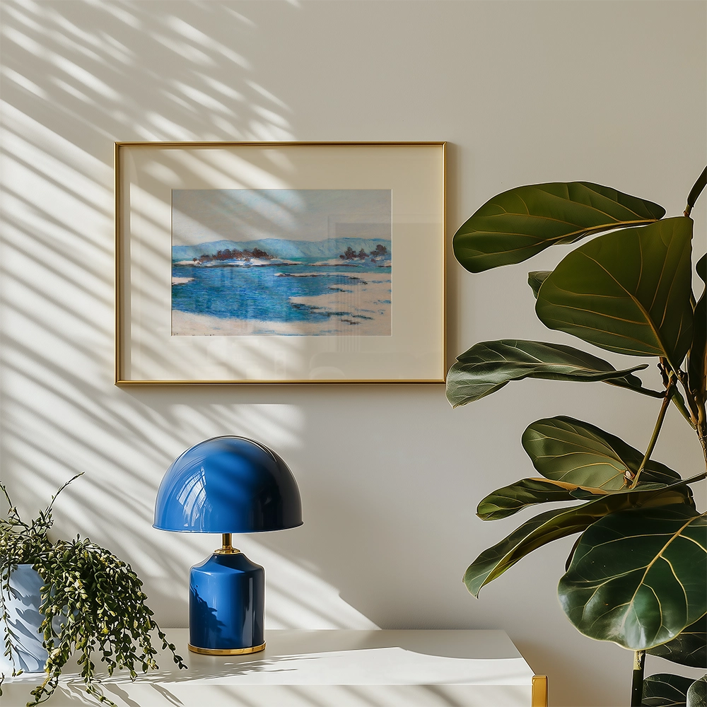 Framed painting of blue water and landscape hanging on a wall next to a blue lamp and green plant.
