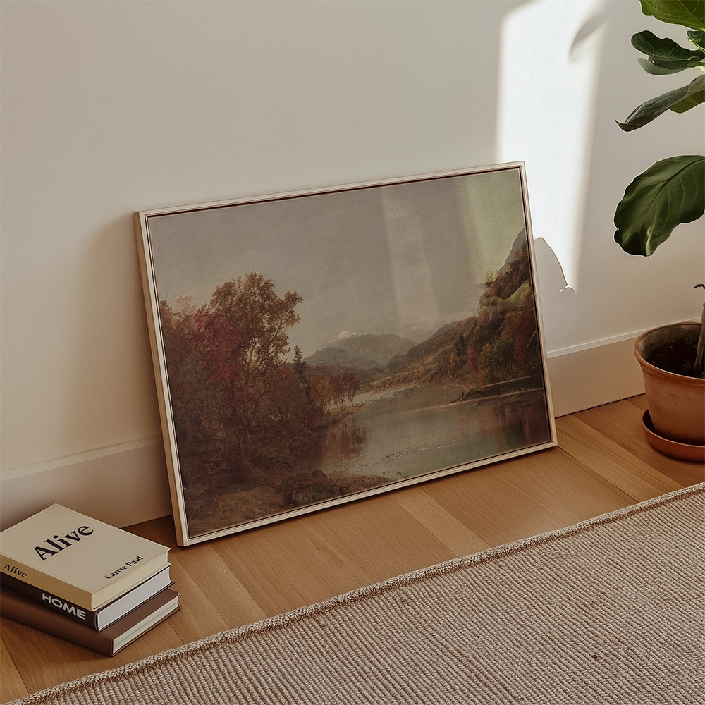 Framed landscape painting propped against a wall, featuring mountains and autumn foliage, with books and a potted plant nearby.