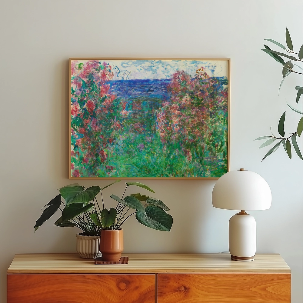 Painting of colorful flowers and a blue sea in a wooden frame, displayed on a light wall above a wooden sideboard with a plant and a lamp.