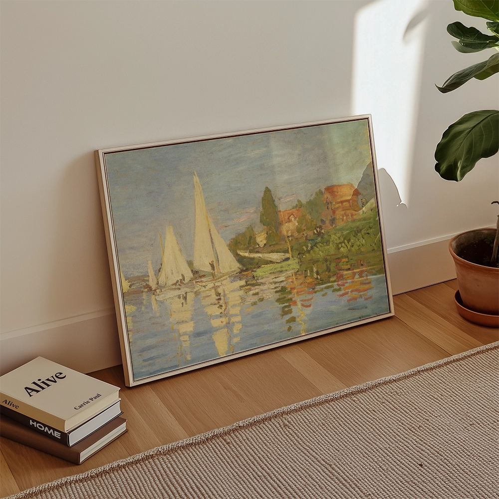 Framed painting of sailboats on water, set in a bright room with books stacked nearby and a potted plant.