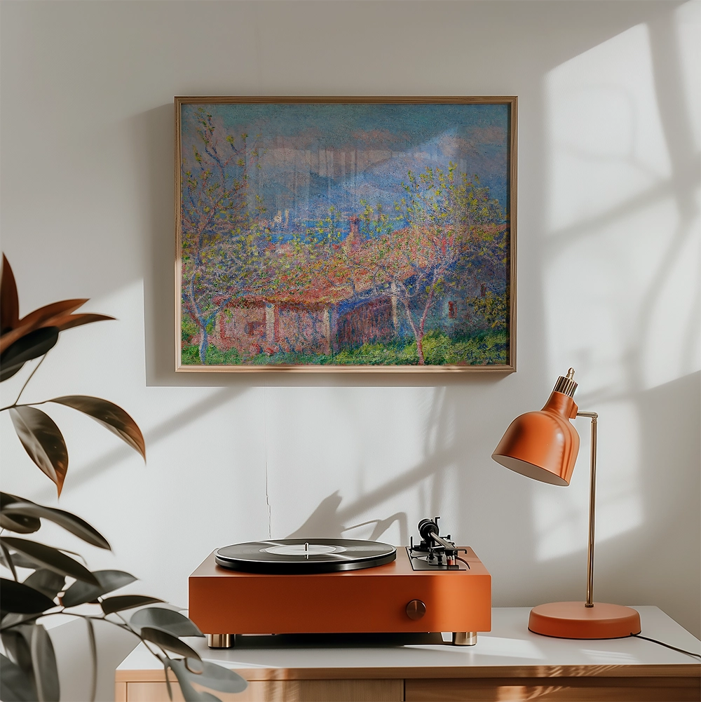 A vibrant landscape painting featuring a rustic building surrounded by trees, displayed in a light wood frame above a stylish orange record player and lamp in a bright, modern interior.