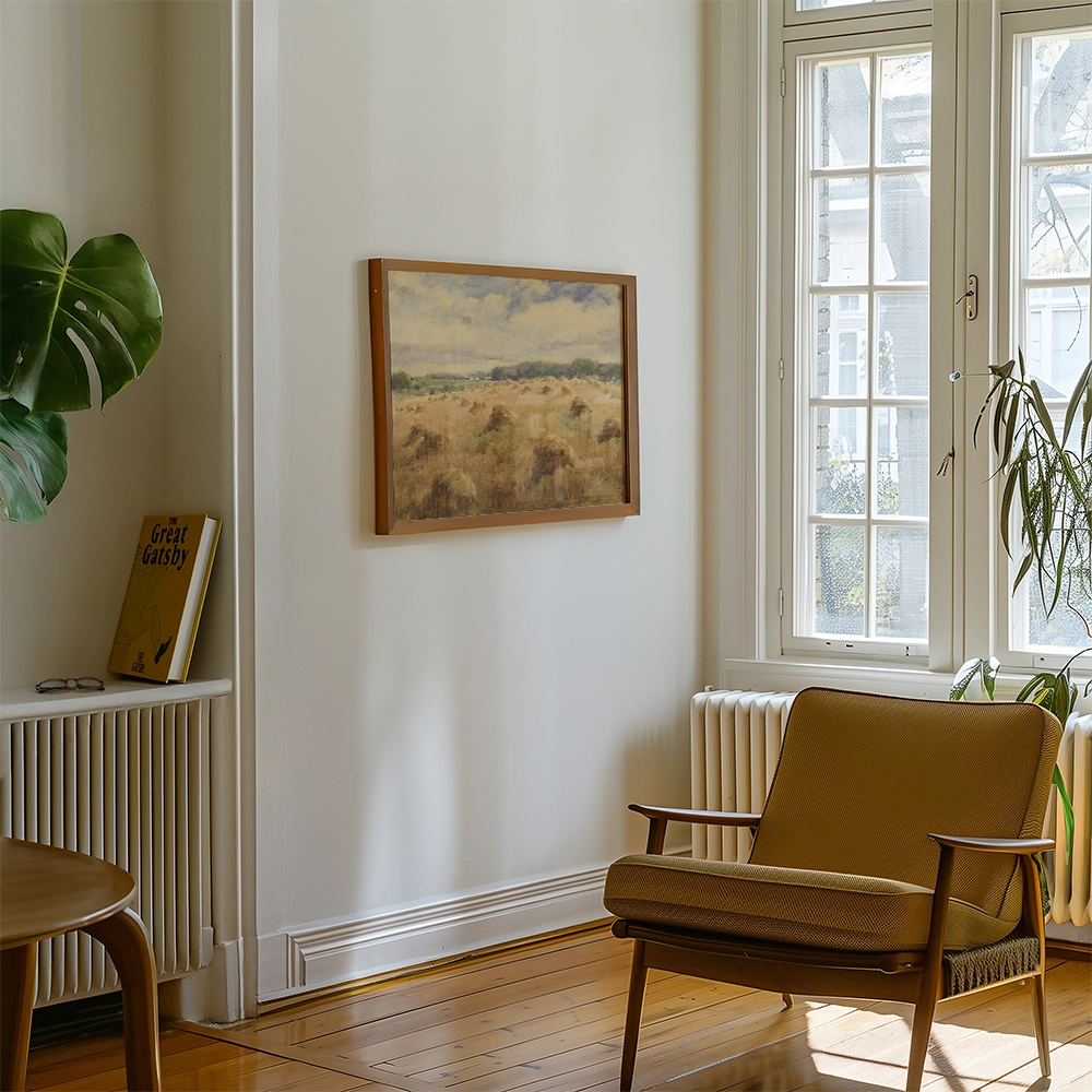 Painting of a serene landscape with fields and clouds, framed and hung on a wall in a cozy room featuring a brown chair and a green plant.