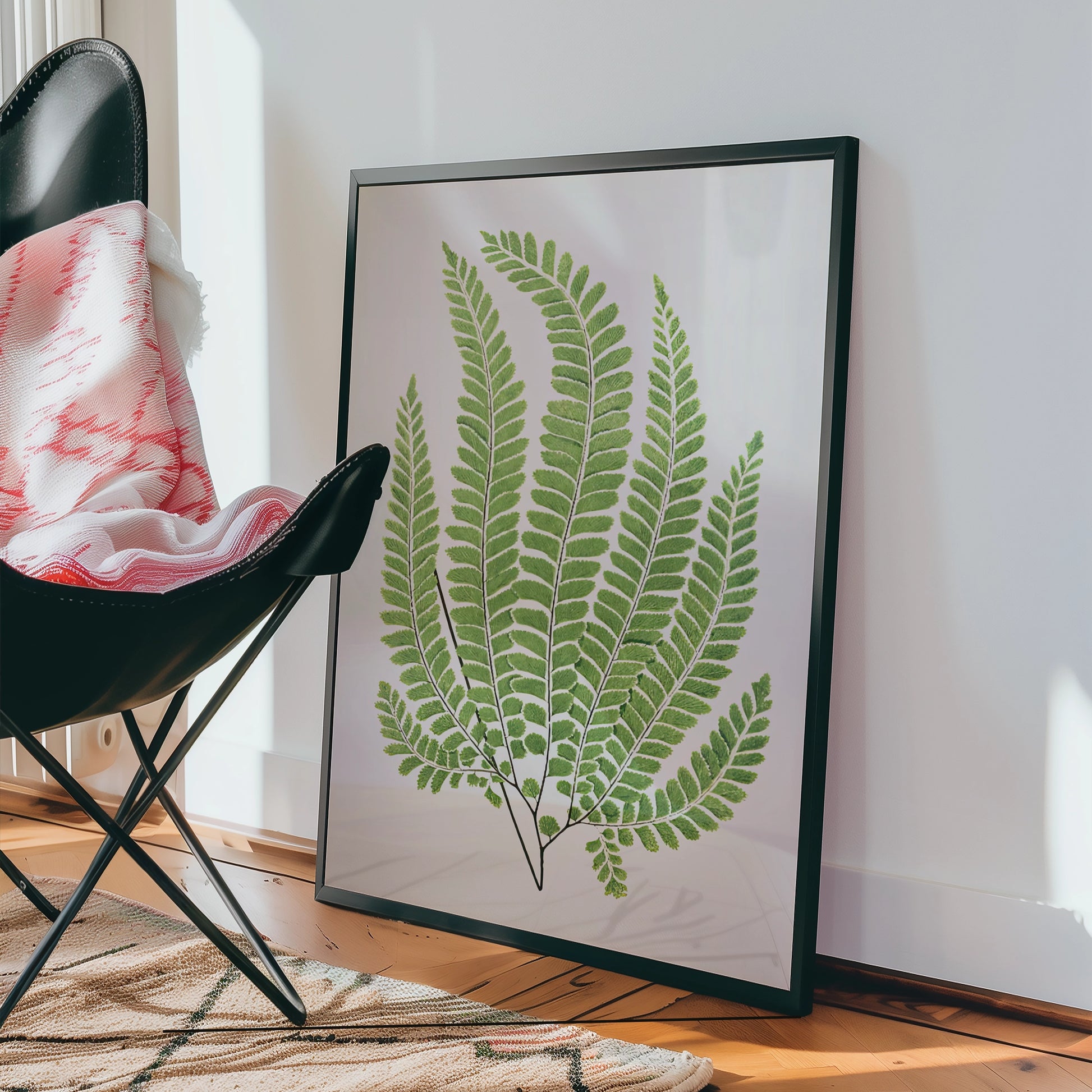 Framed green fern wall art leaning against a wall in a modern interior setting.