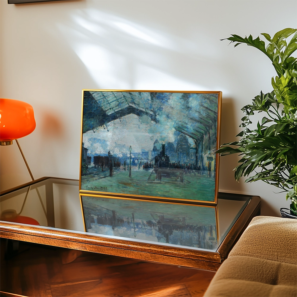 Painting displayed on a wooden table, featuring a blue-toned scene with figures in an indoor space, framed in gold, alongside a potted plant and an orange lamp.