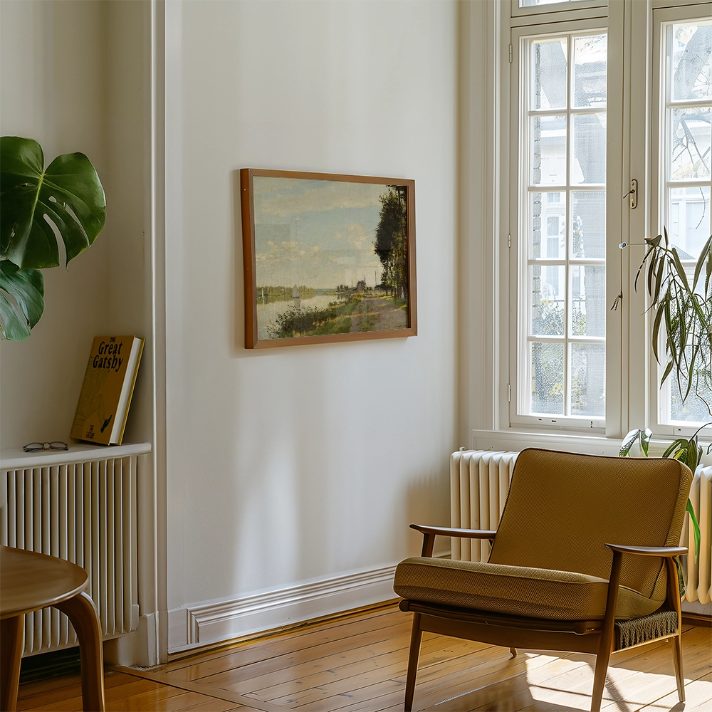 A framed landscape painting hanging on a wall in a bright room with a brown armchair and a green plant nearby