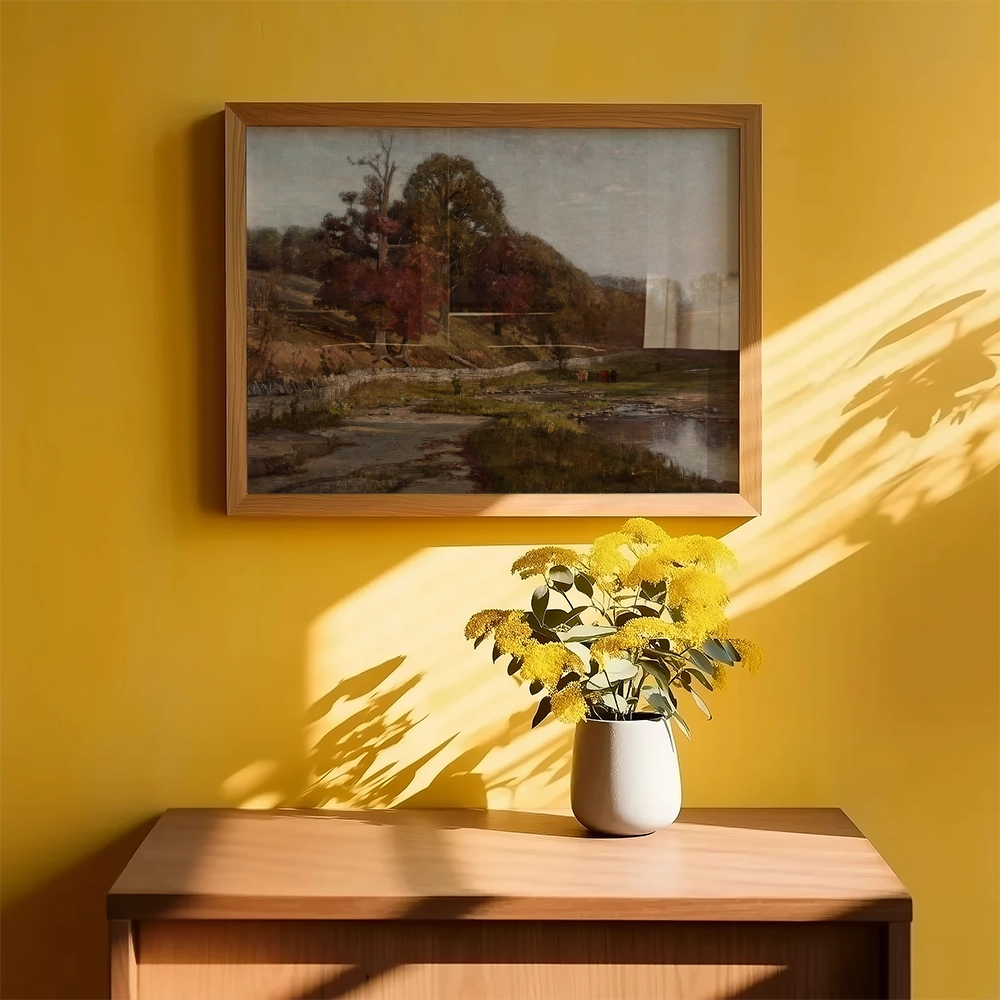Framed landscape painting on a yellow wall with a flower arrangement in a vase on a wooden table.