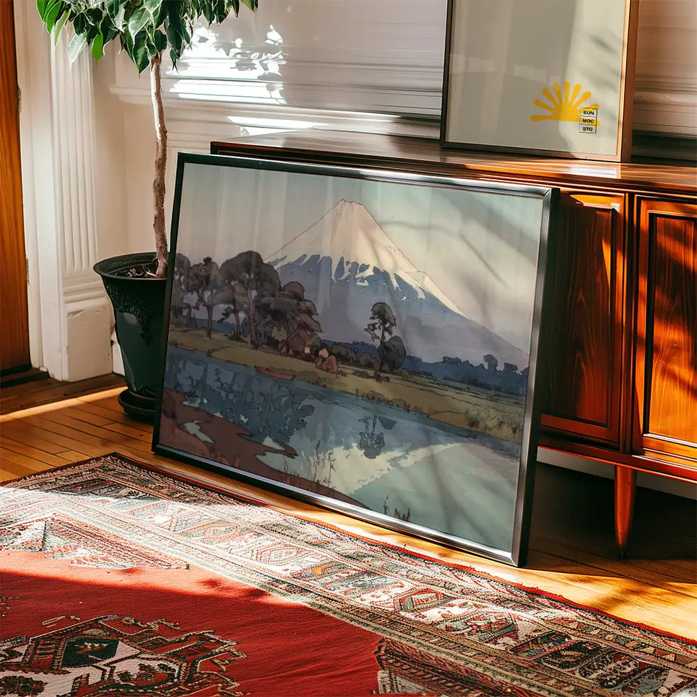 Framed landscape painting featuring a mountain and a serene lake, positioned next to a potted plant in a sunlit room with a patterned rug.