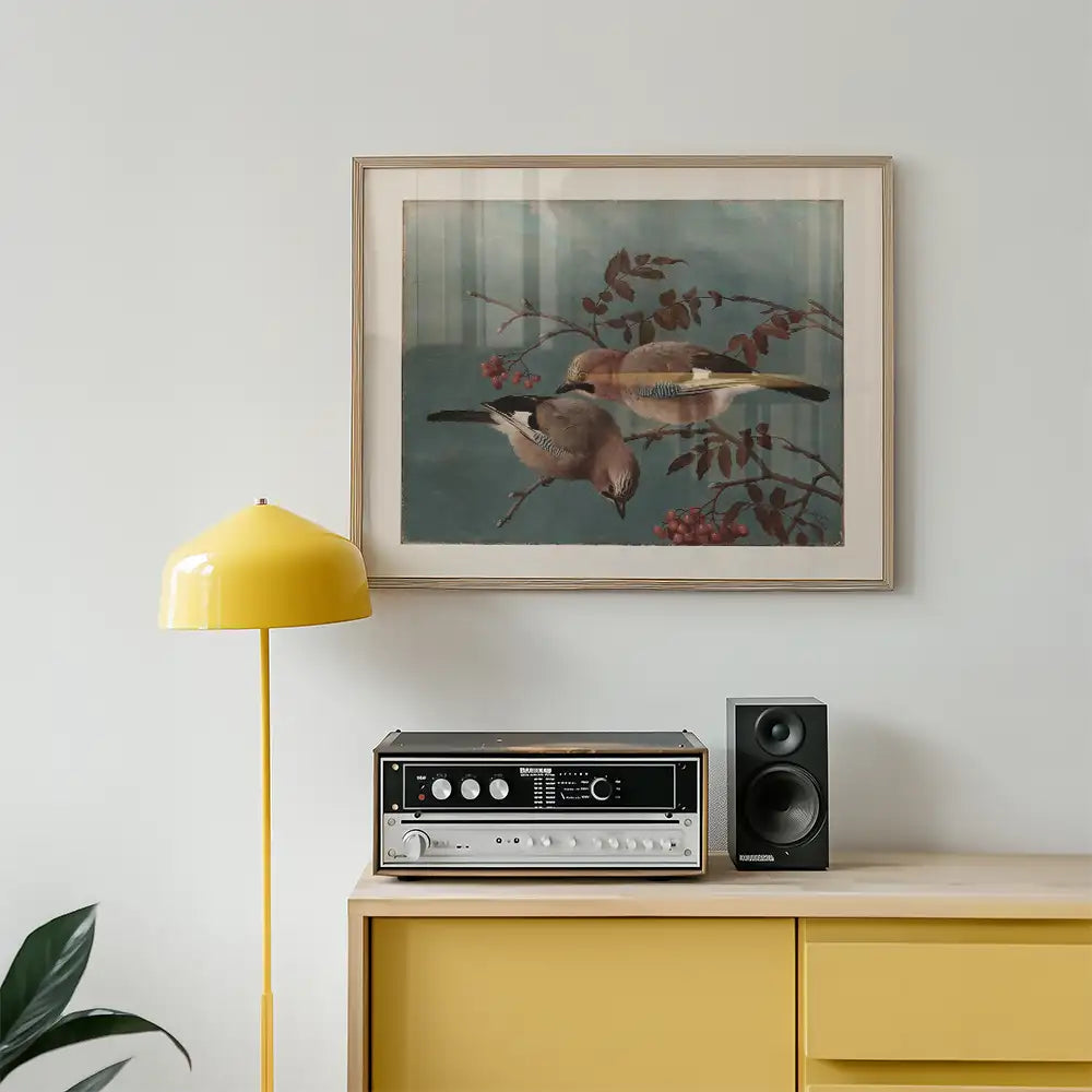 Framed painting of two birds perched on branches with berries, displayed on a wall above a yellow lamp and a vintage record player on a yellow cabinet.