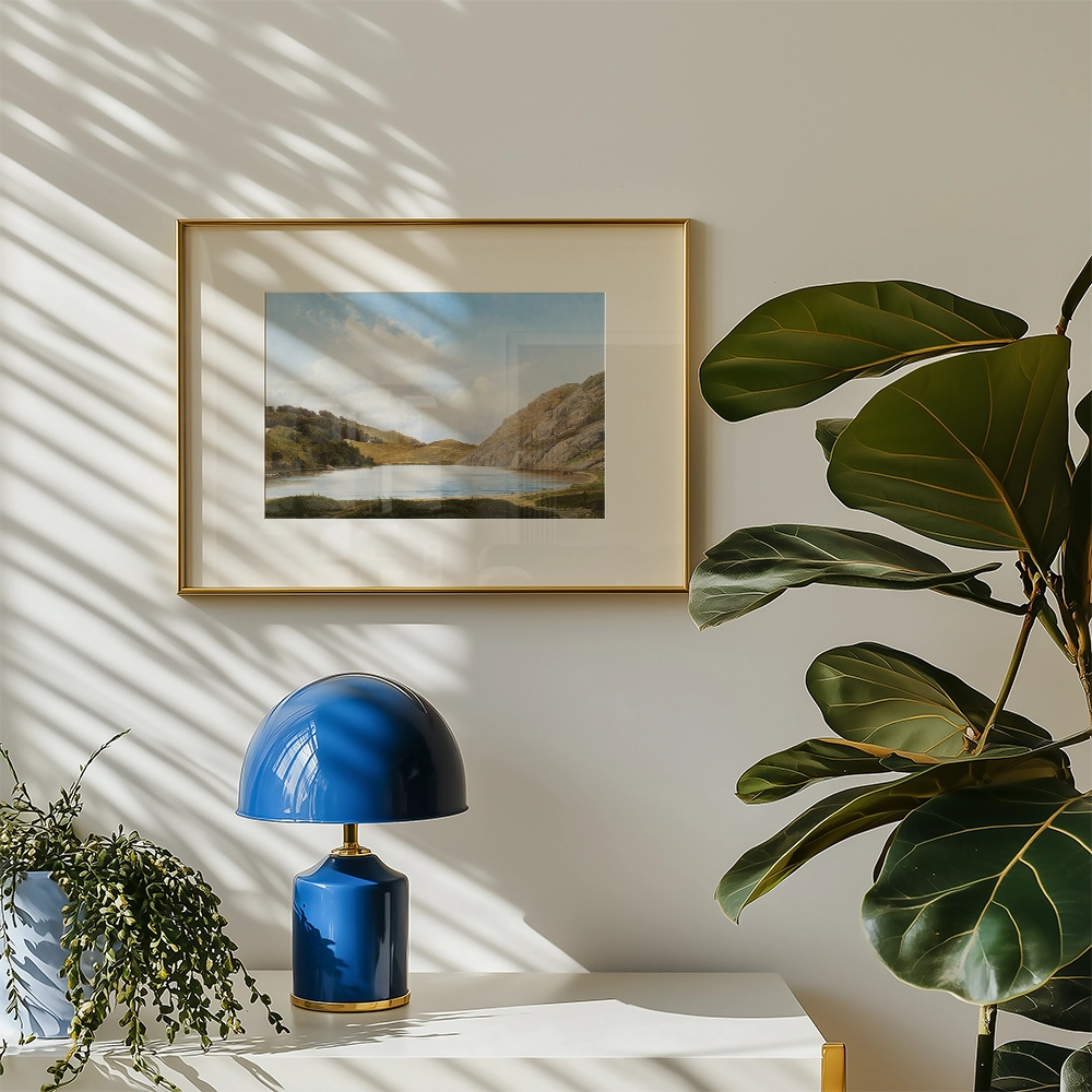 Painting of a serene landscape featuring a lake surrounded by hills, framed in a gold frame, displayed on a wall alongside a blue lamp and a green plant.