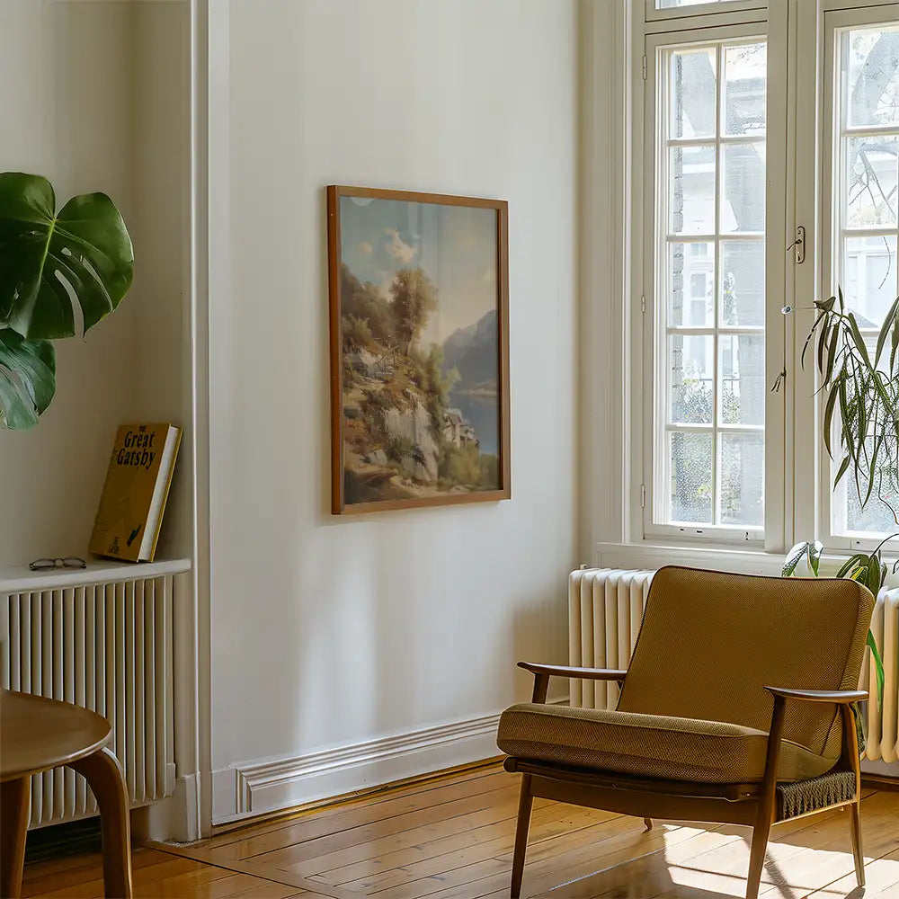 Framed landscape painting on a light wall next to a cozy armchair and a green plant in a sunlit room.