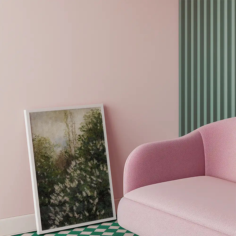 Framed painting of lush greenery leaning against a pink wall, next to a pink sofa.