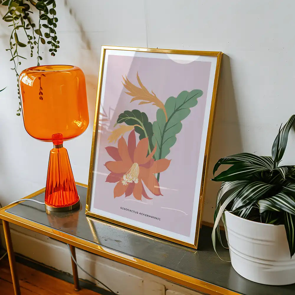 Modern floral art print featuring a Disocactus Ackermannii, framed in gold, displayed on a mid-century style table with an orange lamp and green plants.