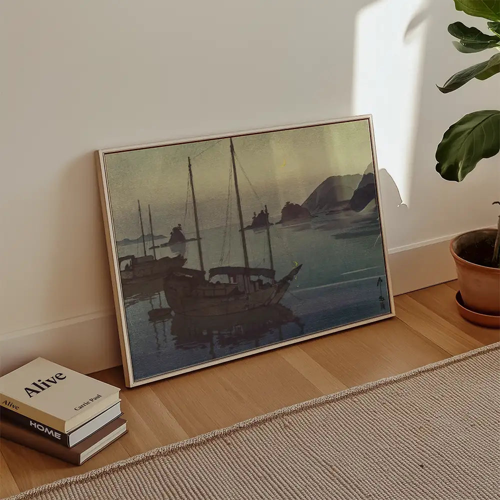 Framed painting of boats on a calm water at sunset, leaning against a wall in a modern living space.