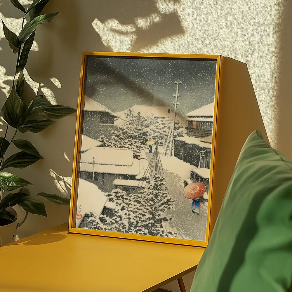 Framed painting of a snowy landscape featuring a person walking with an umbrella, displayed on a yellow table next to a plant.