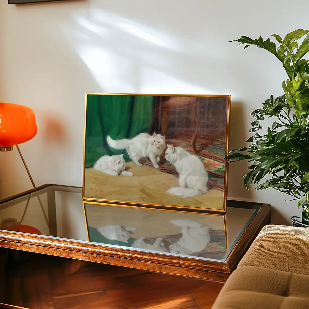 Painting of three white cats interacting on a tan floor, displayed in a gold frame on a glass-topped table, with an orange lamp and green curtain in the background.